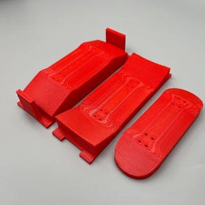 Puede incluir: Tres rampas de fingerboard de plástico rojo, una es una rampa plana, otra es una rampa curva y la última es una rampa de cuarto de tubo.