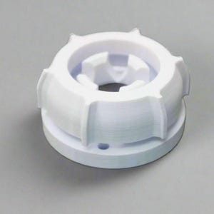 May include: A white, 3D-printed plastic object with a circular design. The object has a base, a central opening, and an outer ring with raised, ridged sections. The design appears to be a mechanical component or part.