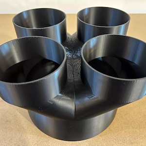 May include: Black plastic 4-into-1 exhaust manifold adapter. The adapter has four round inlets and one larger round outlet.