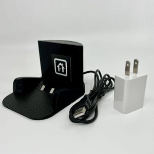 May include: A black charging station with a USB cable and a white wall adapter. The charging station has a small home icon on the front.