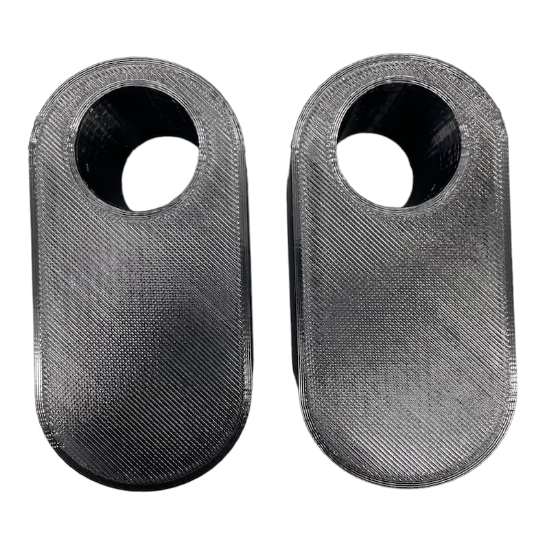 May include: Two gray, 3D-printed, oval-shaped objects with a hole at the top. The objects have a textured surface with diagonal lines. The background is white.