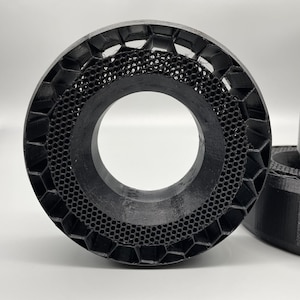 May include: A close-up of a black, 3D printed ring with a honeycomb pattern. The ring is made of a durable plastic material and has a smooth finish.