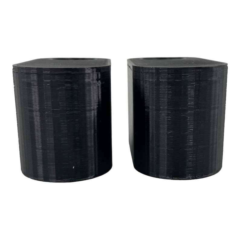 May include: Two black, cylindrical objects with rounded tops and bottoms. The objects are side-by-side, and appear to be 3D-printed. The surface has a textured, layered appearance. The objects are set against a white background.