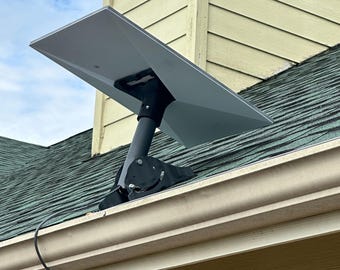 May include: A white satellite dish mounted on a black metal bracket on a roof. The dish is angled upwards and is connected to a cable.