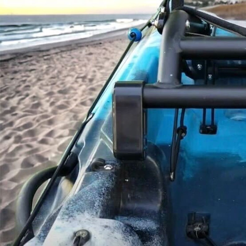 May include: A close-up view of a blue and black kayak with a black metal frame. The kayak is on a sandy beach with the ocean in the background. The kayak has a blue and black color scheme.