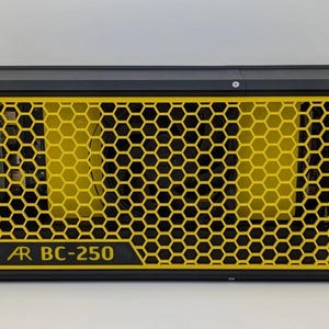 Pode incluir: Dispositivo eletrônico preto e amarelo com um design de grade em favo de mel. O painel frontal apresenta o texto "AR BC-250" em amarelo. O dispositivo tem formato retangular e parece ser um alto-falante ou amplificador.