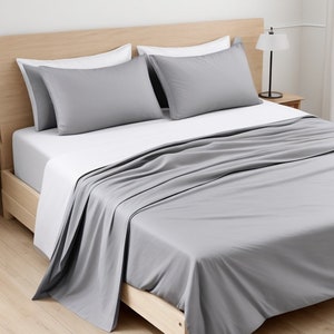 May include: A gray bed sheet set with two gray pillowcases and a white fitted sheet. The bed is made with a wooden frame.