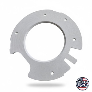 Könnte beinhalten: Ein hellgraues, halbkreisförmiges Metallteil mit einer großen zentralen Öffnung und mehreren kleineren Löchern. Das Teil hat eine strukturierte Oberfläche und einen kleinen Vorsprung auf einer Seite. Die Worte "MADE IN USA" sind auf einem runden Aufkleber aufgedruckt.