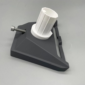 May include: A dark gray 3D-printed object with a white cylindrical component. A silver bolt is attached to the base. The object has a geometric design and appears to be a mechanical part or a tool.