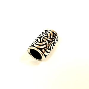 May include: A silver-colored cylindrical bead with a Celtic knot design. The bead has a dark interior and a polished, metallic finish. The intricate pattern covers the entire surface, creating a textured appearance.