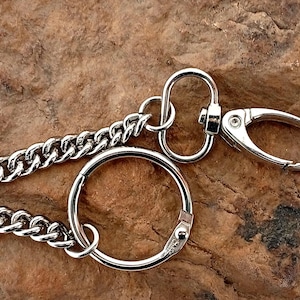 May include: Close-up of a silver-colored keychain with a chain, a large ring, and a clasp. The chain is made of interlocking links. The clasp is oval-shaped and has a spring-loaded mechanism.