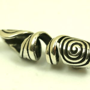 May include: A silver-colored, spiral-shaped finger ring. The ring features a swirling design with a spiral at the end. The ring is made of a shiny, metallic material and is set against a white background.