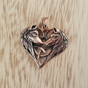 May include: A copper-colored pendant in the shape of a heart, featuring two wolf heads facing each other. The wolves' heads are detailed with fur and facial features. A Celtic knot design is at the bottom of the heart.