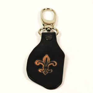 Könnte beinhalten: Schwarzer Leder-Schlüsselanhänger mit silbernem Ring und einem Fleur-de-lis-Design.