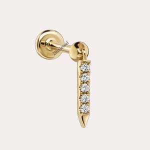 May include: Gold earring with a small diamond-studded bar hanging from it. The earring is a stud style with a small ball at the top.