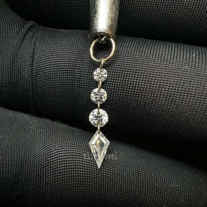 Puede incluir: Primer plano de una joya plateada con cuatro diamantes claros y brillantes. Tres diamantes redondos est&aacute;n unidos, con un diamante en forma de cometa en la parte inferior. La joya est&aacute; suspendida de un lazo plateado.