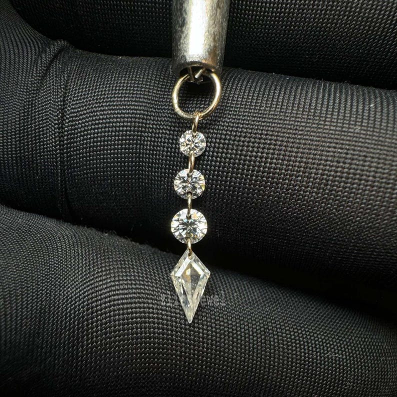 Puede incluir: Primer plano de una joya plateada con cuatro diamantes claros y brillantes. Tres diamantes redondos est&aacute;n unidos, con un diamante en forma de cometa en la parte inferior. La joya est&aacute; suspendida de un lazo plateado.