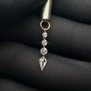 Puede incluir: Primer plano de una joya plateada con un anillo dorado y una serie de cristales claros y brillantes. Los cristales son redondos y en forma de diamante, suspendidos verticalmente.