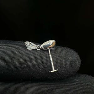 Puede incluir: Un solo pendiente de plata con una gema clara y facetada y un poste. El pendiente se muestra sobre una superficie negra. El texto "Zlissjewel" es visible en el pendiente.