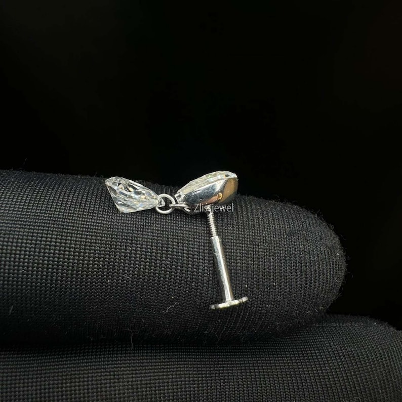 Puede incluir: Un solo pendiente de plata con una gema clara y facetada y un poste. El pendiente se muestra sobre una superficie negra. El texto "Zlissjewel" es visible en el pendiente.