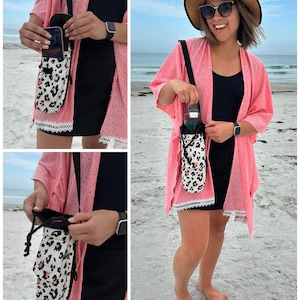 May include: A crossbody bag with a black strap and a white and tan leopard print pouch. The pouch has a drawstring closure and a pocket. The bag is being held by a person on a beach.