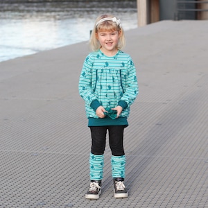 May include: A young girl wearing a teal and white striped long-sleeved shirt with a teal and white striped leg warmers and black sneakers.