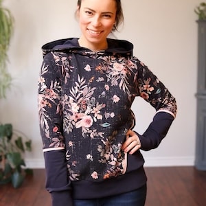 Puede incluir: Una sudadera con capucha azul marino con estampado floral. La sudadera tiene una capucha azul oscuro y una banda azul oscuro alrededor de la parte inferior. Las mangas son de color azul oscuro.