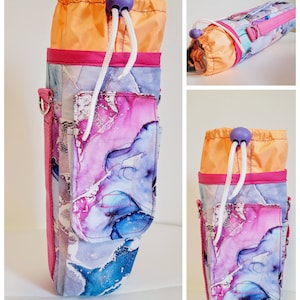 May include: A water bottle holder with a vibrant abstract design in shades of blue, purple, and white. The holder features a drawstring closure with a purple bead, a pink trim, and a side pocket. The top is orange.