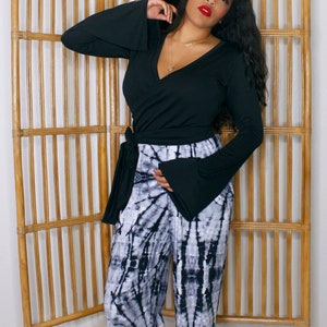Puede incluir: Una mujer con un top negro de manga larga con cuello en V, mangas acampanadas y detalle de lazo, combinado con pantalones tie-dye en blanco y negro.