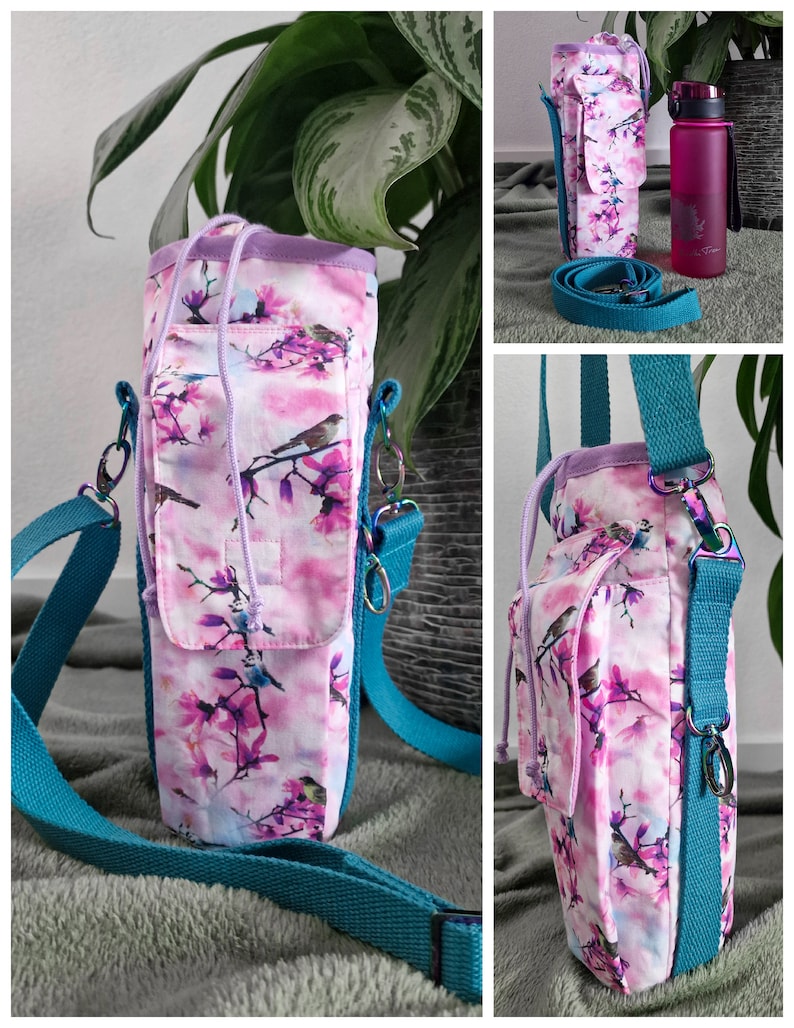 May include: A floral water bottle carrier with a teal strap. The carrier features a pink and white floral pattern with birds. The carrier has a small pocket and a drawstring closure. A pink water bottle is also visible.