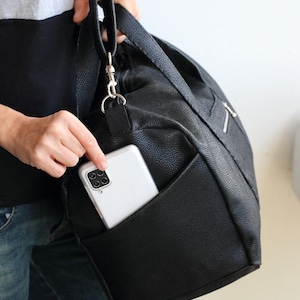 The handmade duffle bag is made of black waterproof canvas, showcasing its side slip exterior pocket and adjustable strap.