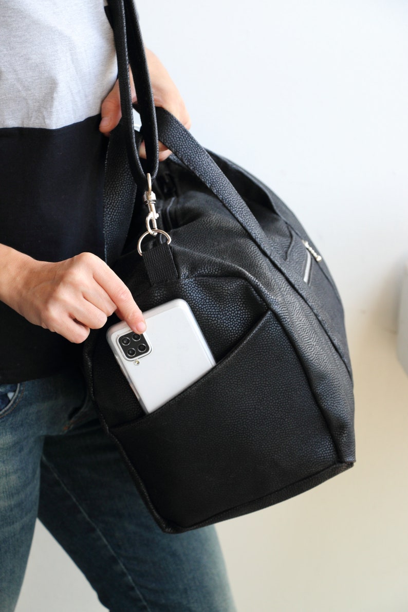 The handmade duffle bag is made of black waterproof canvas, showcasing its side slip exterior pocket and adjustable strap.