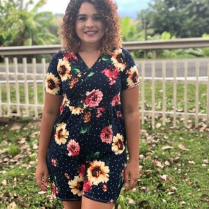 Puede incluir: Una mujer con un vestido azul marino con estampado floral y lunares blancos. El vestido tiene mangas cortas y un escote en V.