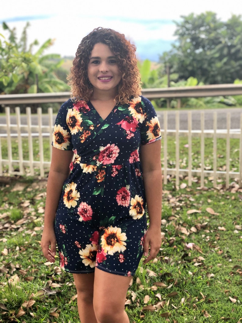 Puede incluir: Una mujer con un vestido azul marino con estampado floral y lunares blancos. El vestido tiene mangas cortas y un escote en V.