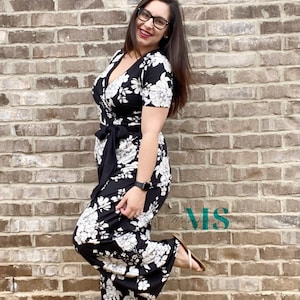 Puede incluir: Una mujer con un mono negro y blanco con estampado floral, cuello en V y mangas cortas. Est&aacute; de pie frente a una pared de ladrillo y tiene el pie sobre un ladrillo.
