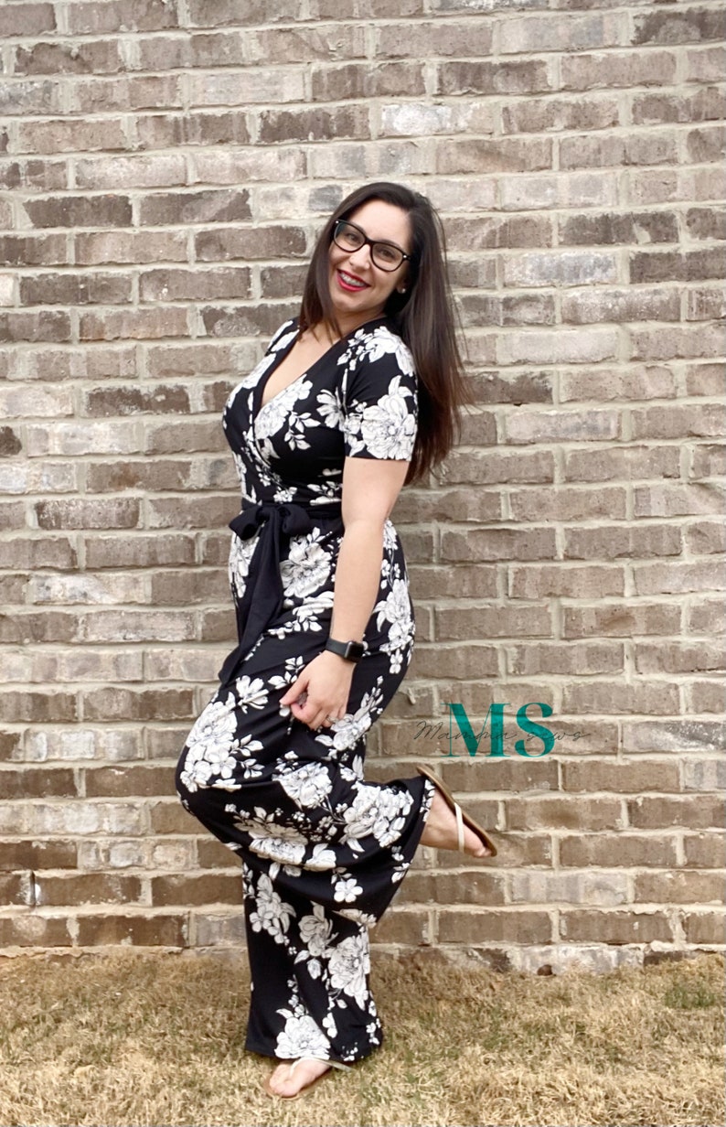 Puede incluir: Una mujer con un mono negro y blanco con estampado floral, cuello en V y mangas cortas. Est&aacute; de pie frente a una pared de ladrillo y tiene el pie sobre un ladrillo.
