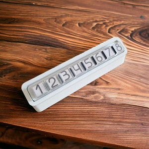 Può includere: Display di numeri in plastica bianca con i numeri da 1 a 8 visibili. Il display è su una superficie di legno.