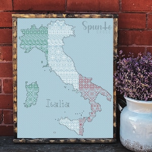 May include: A cross-stitch pattern of Italy, with the Italian flag colours represented in the design. The pattern is framed in a brown wooden frame and the word "Italia" is stitched in the centre.