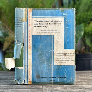 May include: Vintage book titled "Conduction, Infiltration and General Anesthesia in Dentistry" by Mendel Nevin and P.G. Puterbaugh. The book has a blue cover with white text and a worn appearance. The edition is marked as "Revised Fourth Edition 1946".