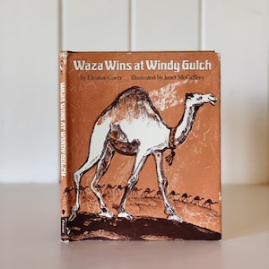 May include: A vintage children's book cover with a brown background and a camel illustration. The title of the book is "Waza Wins at Windy Gulch" by Eleanor Coerr, illustrated by Janet McCaffery.