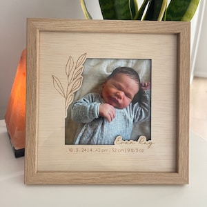 May include: A wooden photo frame with a light brown finish. The frame has a cutout design of a leafy branch. A photo of a baby boy is in the frame. The baby is wearing a light blue onesie. The frame also includes the baby's name, "Evan Ray", and birth details: "18.3.24 | 4:42 pm | 52 cm | 9 lb 3 oz".