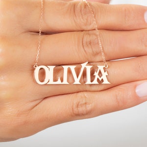 May include: A gold necklace with the name "Olivia" spelled out in bold letters.