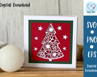 Puede incluir: Una tarjeta blanca con un borde rojo y verde, que presenta un recorte blanco de un árbol de Navidad con detalles florales. El árbol está rodeado de estrellas blancas. La tarjeta está sobre una superficie de madera con un adorno navideño blanco.