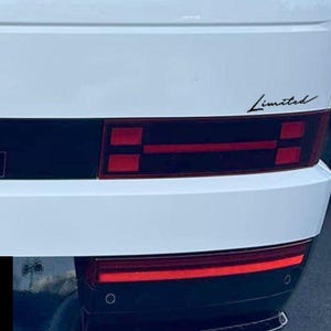 May include: Rear view of a white vehicle with a black accent panel and red taillights. The word "Limited" is written in a cursive font on the right side of the vehicle.