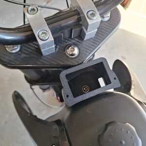 May include: Close-up of motorcycle handlebars and components. The image shows a black handlebar, silver clamps, and a black carbon fiber-textured panel. A black rectangular component with a hole is also visible.