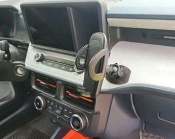 Puede incluir: Un soporte para teléfono de coche negro con una cabeza giratoria y una base de ventosa. El soporte está fijado al salpicadero de un coche.