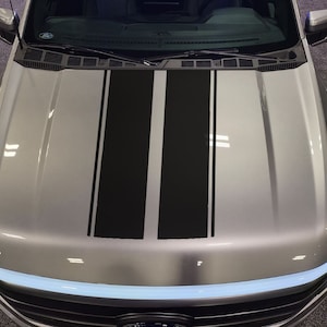 May include: A silver pickup truck with black racing stripes down the hood.