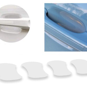 May include: White car door handle protectors. The image shows a close-up of a white car door handle, a car door with a handle, and four white adhesive protectors. The protectors are shaped to fit the door handle recess.