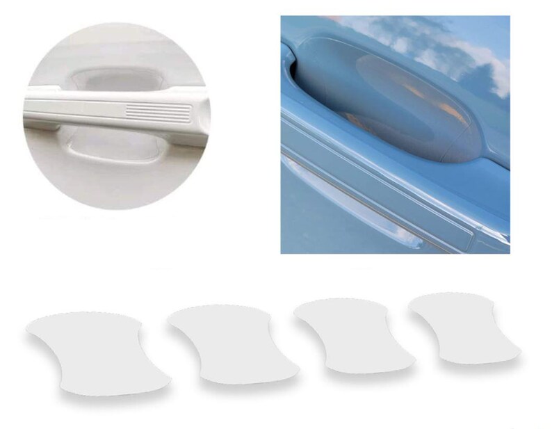 May include: White car door handle protectors. The image shows a close-up of a white car door handle, a car door with a handle, and four white adhesive protectors. The protectors are shaped to fit the door handle recess.