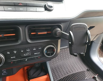 Puede incluir: Un soporte de teléfono para coche negro fijado a la ventilación de un coche. El soporte tiene un brazo giratorio y un soporte de teléfono de resorte.